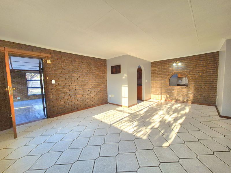 Spacious living area featuring exposed brick walls, unique hexagonal floor tiling, and an open archway leading to adjacent rooms.