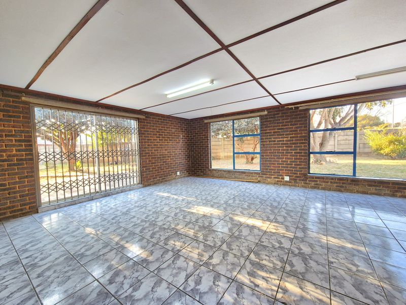 Spacious living area featuring exposed brick walls, tiled flooring, and large windows with security gates, offering a bright and open blank canvas.