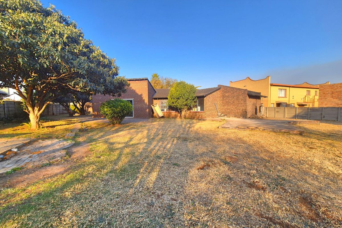 Rear view of the property featuring a brick facade, a paved patio area, and a spacious garden with established trees.