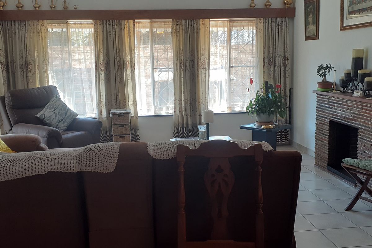 A comfortable living room featuring a brick fireplace, tiled flooring, and large windows with natural light.