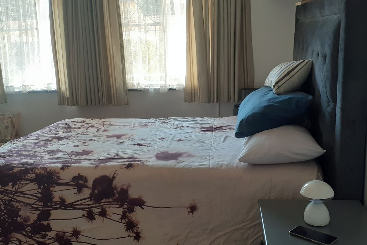 A functional bedroom featuring tiled flooring and large windows with installed curtain tracks, providing natural light to the space.