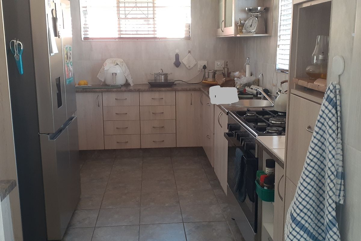A functional kitchen featuring light-toned cabinetry, tiled flooring, a gas stove, and a stainless steel sink with tiled splashbacks.