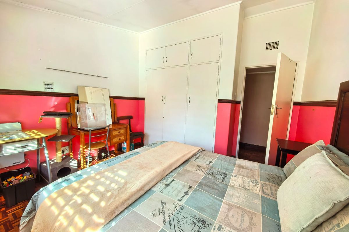 A bedroom featuring built-in cupboards, parquet flooring, and a ventilation grille, currently requiring cosmetic updates to the wall finishes.