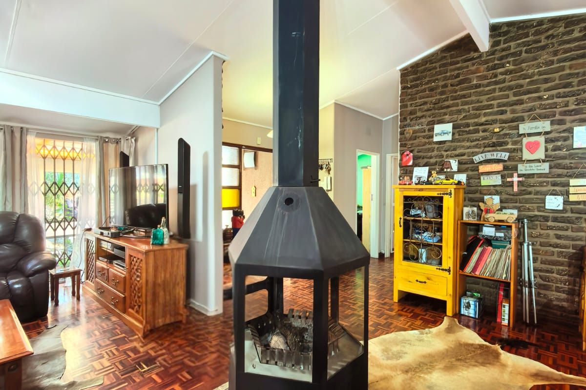 Spacious living room featuring a central freestanding fireplace, vaulted ceilings with exposed beams, and classic parquet flooring, complemented by an exposed brick feature wall.