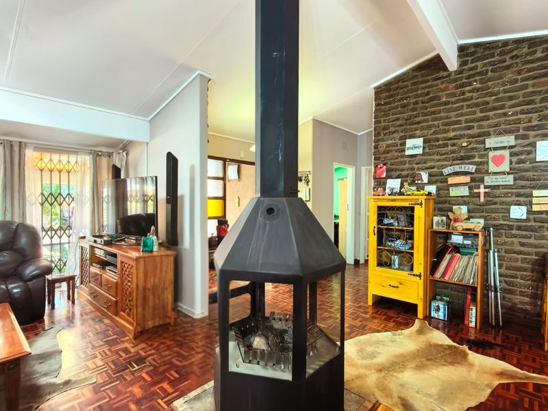 Spacious living room featuring a central freestanding fireplace, vaulted ceilings with exposed beams, and classic parquet flooring, complemented by an exposed brick feature wall.