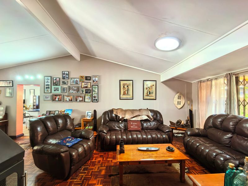Spacious living room featuring vaulted ceilings with exposed beams, classic parquet flooring, and natural light through a window with security gate.