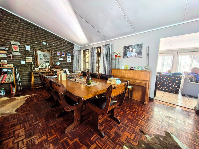 Spacious dining room featuring a vaulted ceiling, exposed brick feature wall, and traditional parquet flooring, with an open flow into the adjacent living area.