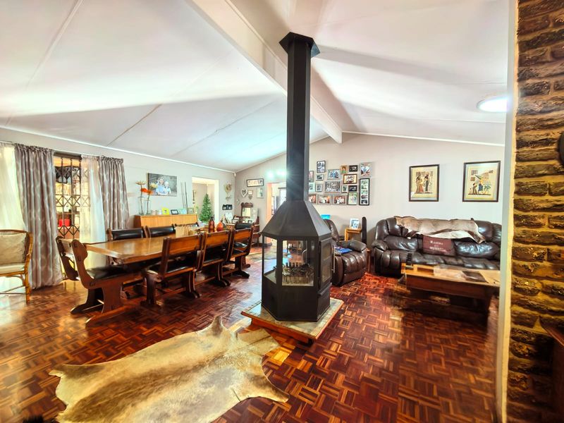 Spacious open-plan living and dining area featuring a central freestanding fireplace, vaulted ceilings, and classic parquet flooring throughout.