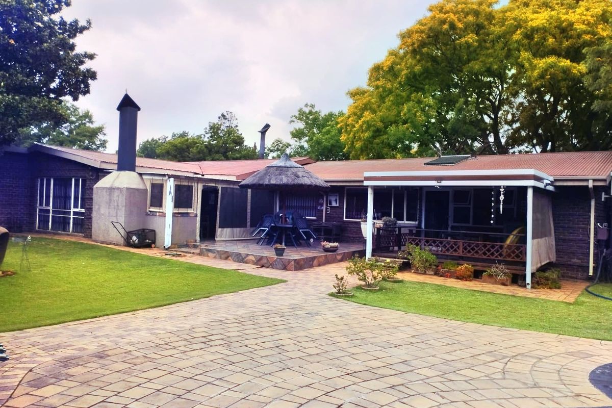Rear view of the property featuring a brick facade, covered patio area, outdoor fireplace, paved courtyard, and a swimming pool set within a garden.