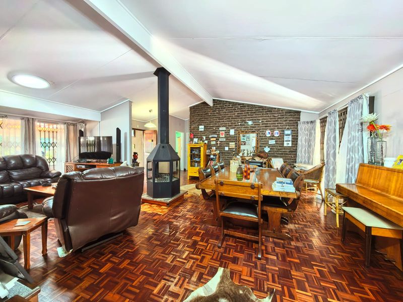 Spacious open-plan living and dining area featuring a striking central freestanding fireplace, exposed brick feature wall, and classic parquet flooring under a vaulted ceiling.