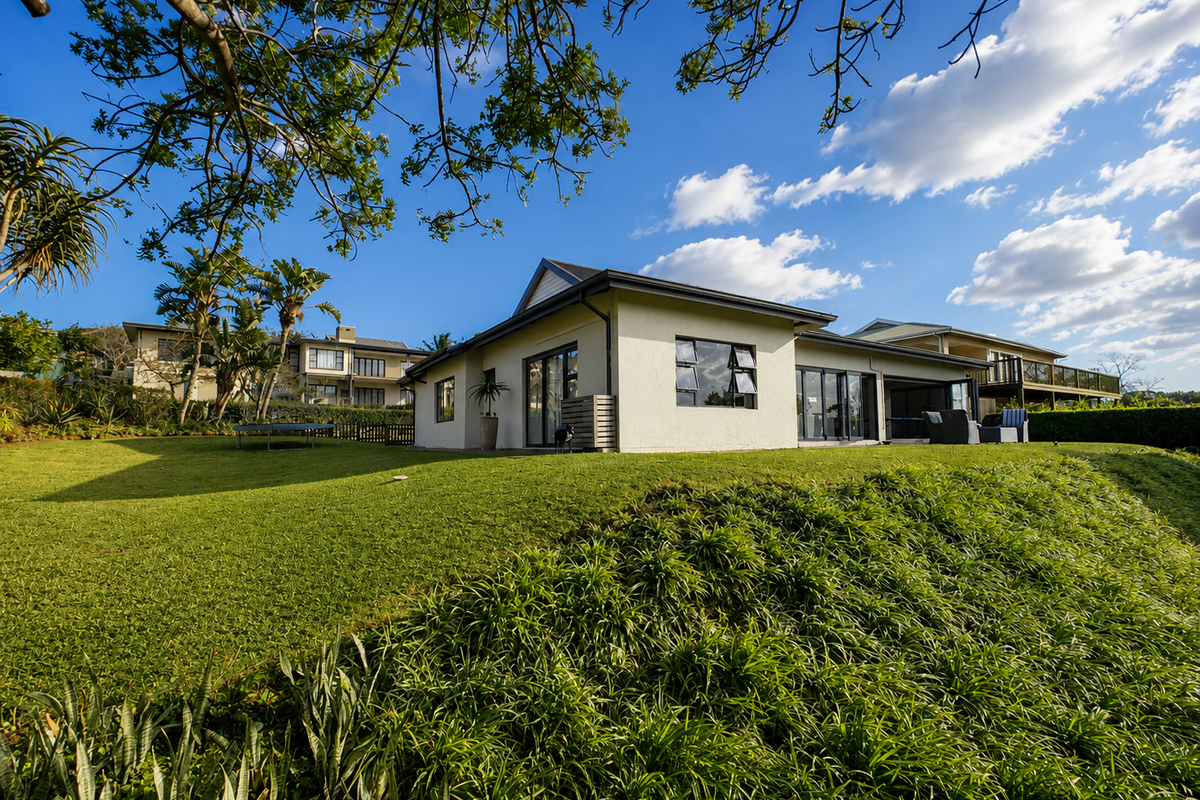 A well-maintained rear exterior view of the house featuring a spacious lawn, landscaped garden, and modern sliding glass doors leading to a patio area.