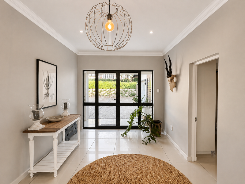 Bright and welcoming entrance hall featuring polished tile flooring, modern crown molding, and a large glass-paneled door providing natural light and garden views.