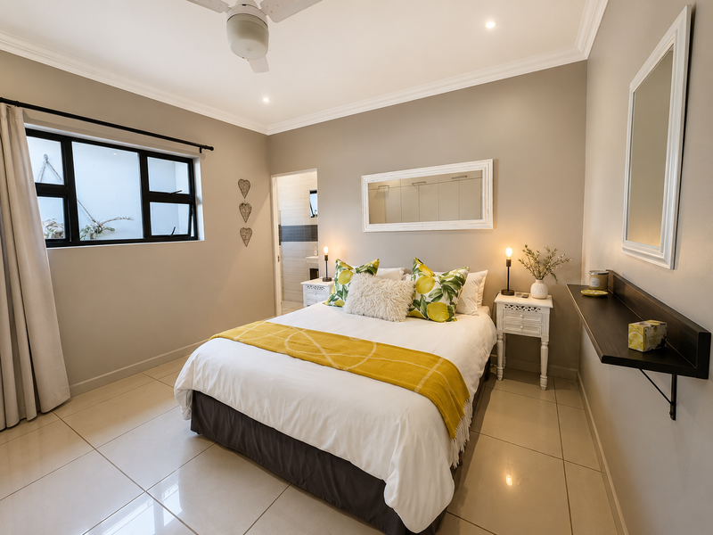 A well-maintained bedroom featuring neutral wall tones, large format floor tiles, a ceiling fan, and direct access to an en-suite bathroom.