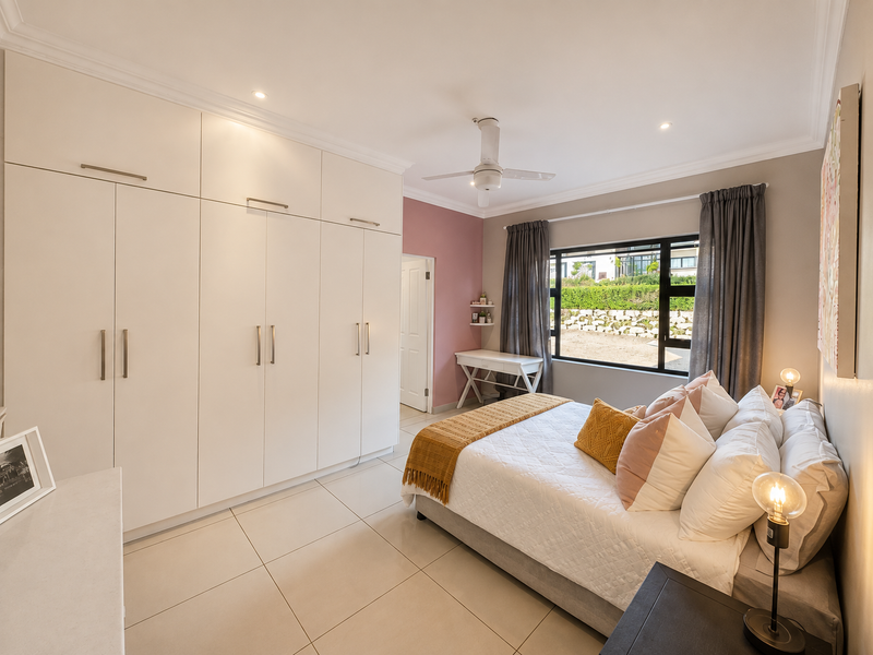A well-maintained bedroom featuring extensive built-in cupboards, tiled flooring, a ceiling fan, and large windows allowing for natural light.