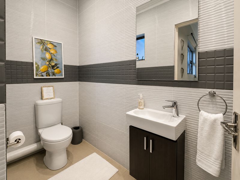 A modern guest bathroom featuring contemporary wall tiling, a compact vanity with a ceramic basin, and a dual-flush toilet.