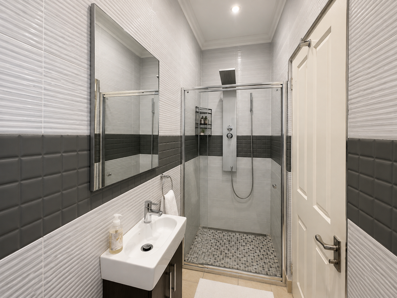 Modern bathroom featuring a glass-enclosed shower with a rainfall shower panel, wall-mounted vanity basin, and contemporary textured wall tiling.