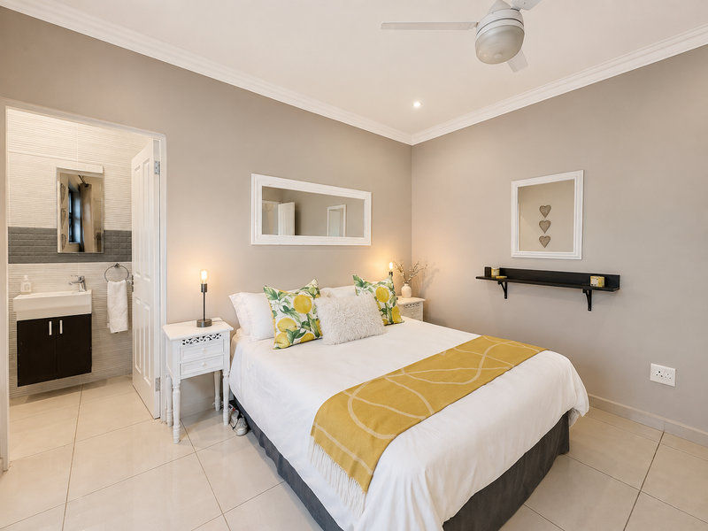 A well-maintained bedroom featuring neutral tones, tiled flooring, a ceiling fan, and an adjoining en-suite bathroom with a modern vanity basin.