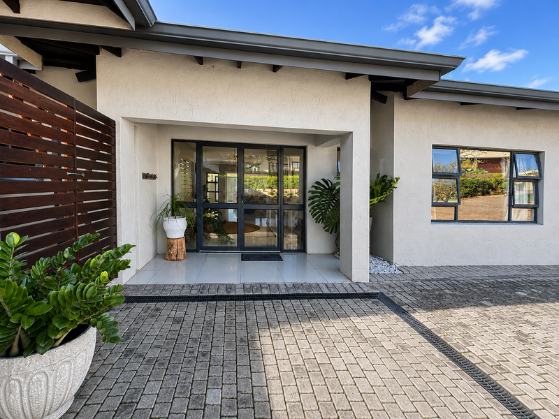 Modern front entrance featuring a paved driveway, tiled porch, timber privacy screen, and contemporary aluminium-framed glass door and windows.