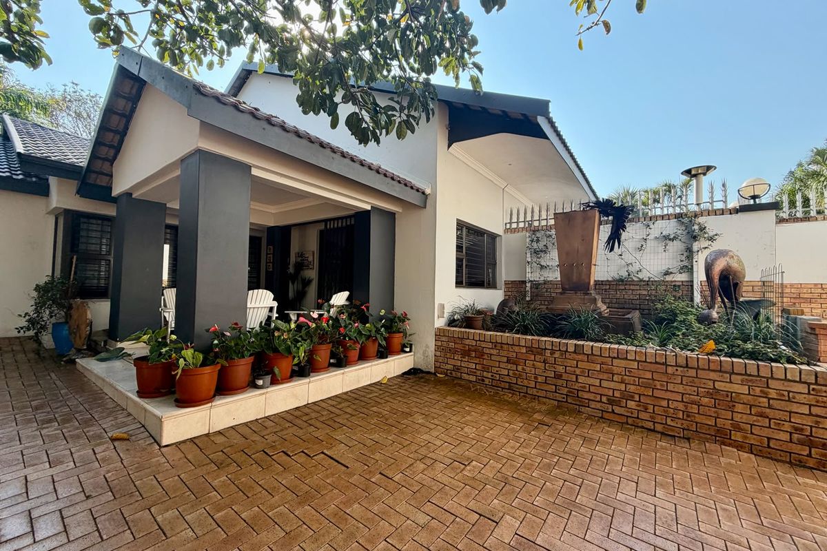 A well-maintained rear exterior featuring a covered patio, brick-paved courtyard, and a decorative brick-walled water feature.