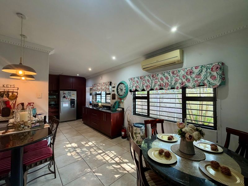 Open-plan kitchen and dining area featuring dark wood cabinetry, tiled floors, and large windows with security bars, offering a functional and connected living space.