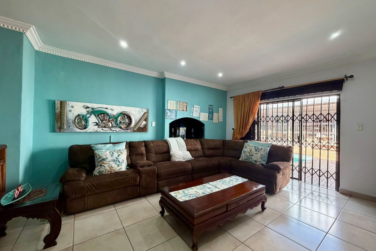 A spacious living room featuring ceramic floor tiles, recessed lighting, decorative crown molding, and a sliding glass door with security gate leading to the exterior.