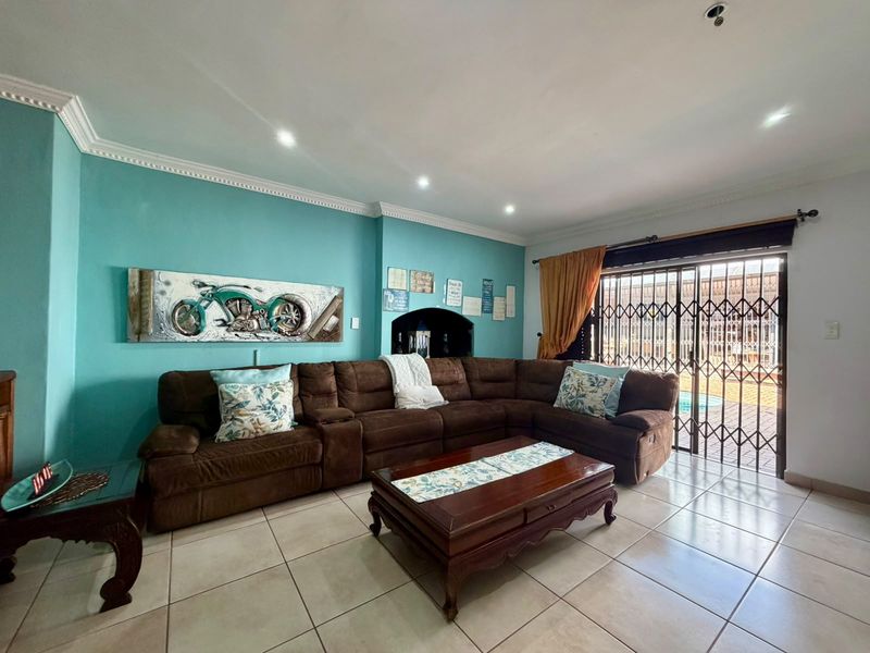 A spacious living room featuring ceramic floor tiles, recessed lighting, decorative crown molding, and a sliding glass door with security gate leading to the exterior.