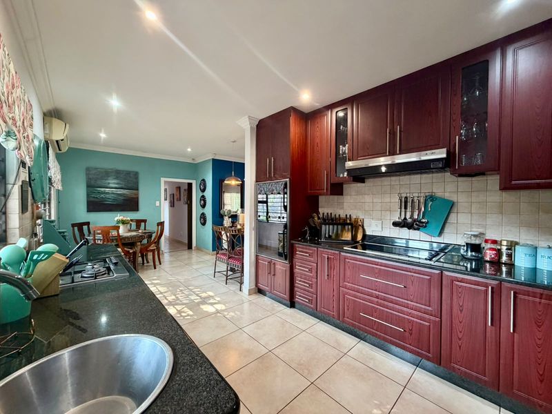 Open-plan kitchen featuring dark wood cabinetry, granite countertops, and integrated appliances, flowing into a dining area with tiled flooring throughout.