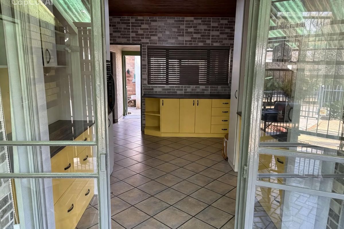 A functional kitchen space featuring yellow cabinetry, dark laminate countertops, tiled flooring, and a brick-style feature wall with timber ceiling accents.
