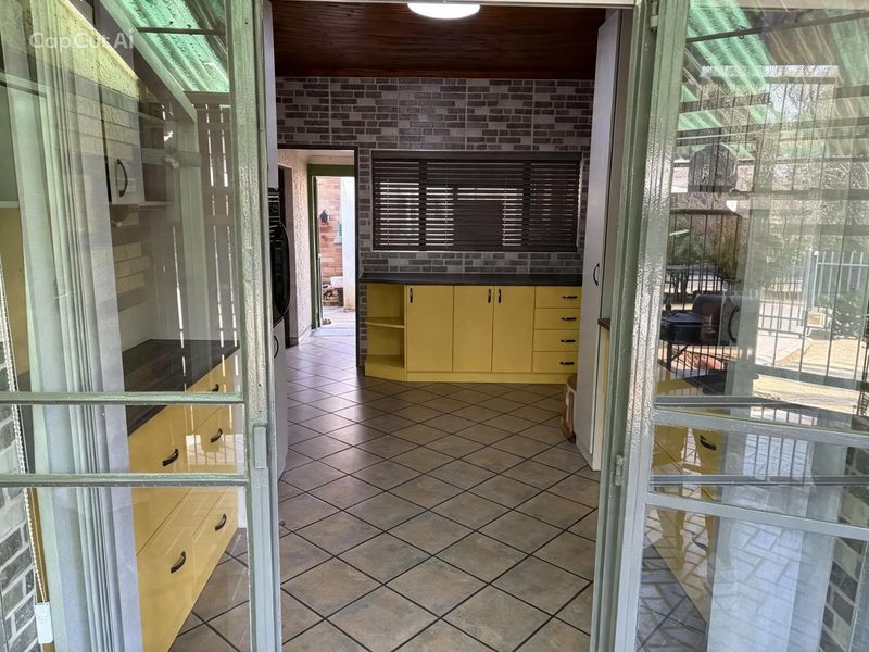 A functional kitchen space featuring yellow cabinetry, dark laminate countertops, tiled flooring, and a brick-style feature wall with timber ceiling accents.