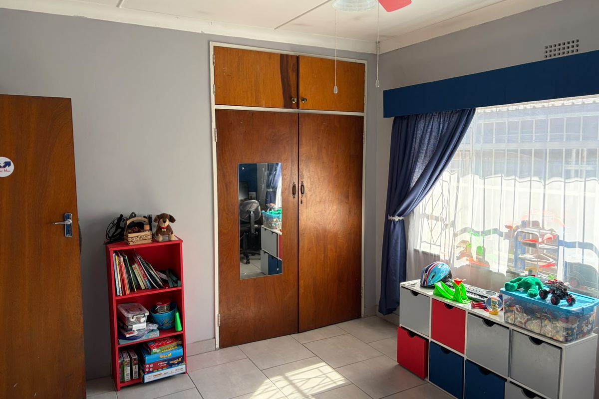 A bedroom featuring tiled flooring, a ceiling fan, and a built-in wooden wardrobe with integrated storage.