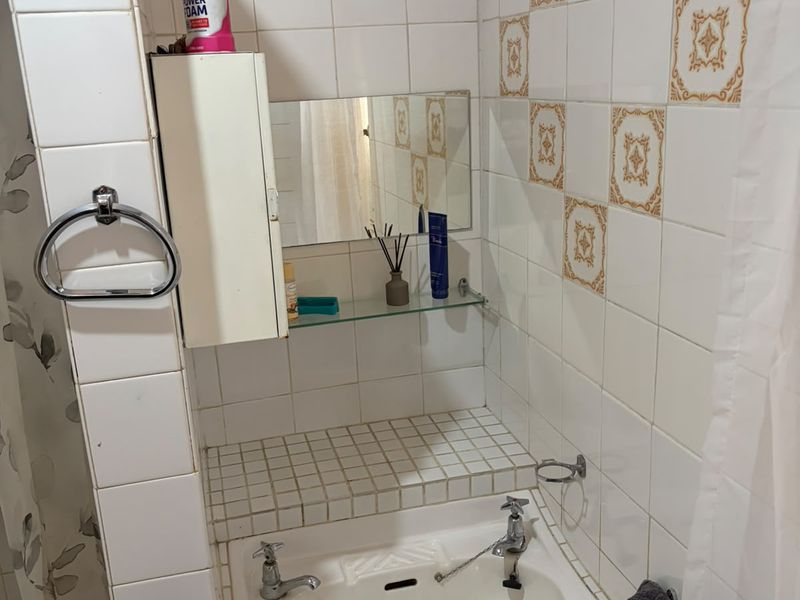 A compact bathroom featuring a wall-mounted basin with tiled splashback, built-in medicine cabinet, and shower area with curtain rail.