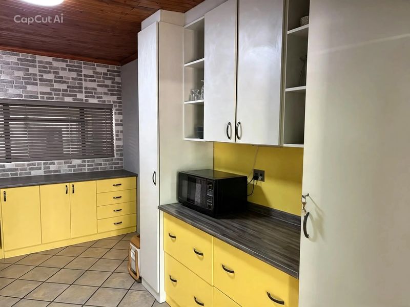 A functional kitchen featuring yellow cabinetry, dark laminate countertops, brick-effect wall accents, and a timber ceiling.