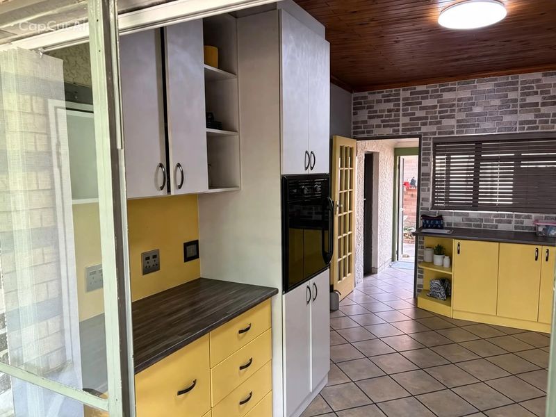 A functional kitchen featuring yellow cabinetry, dark laminate countertops, tiled flooring, and a timber-paneled ceiling with a brick-style feature wall.