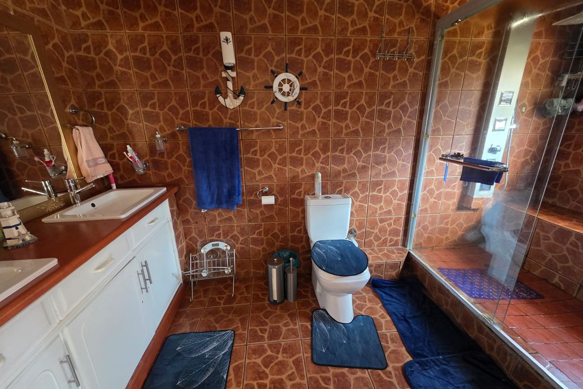 A functional bathroom featuring a vanity cabinet with a basin, a toilet, and a glass-enclosed shower, finished with dated brown patterned wall and floor tiles.