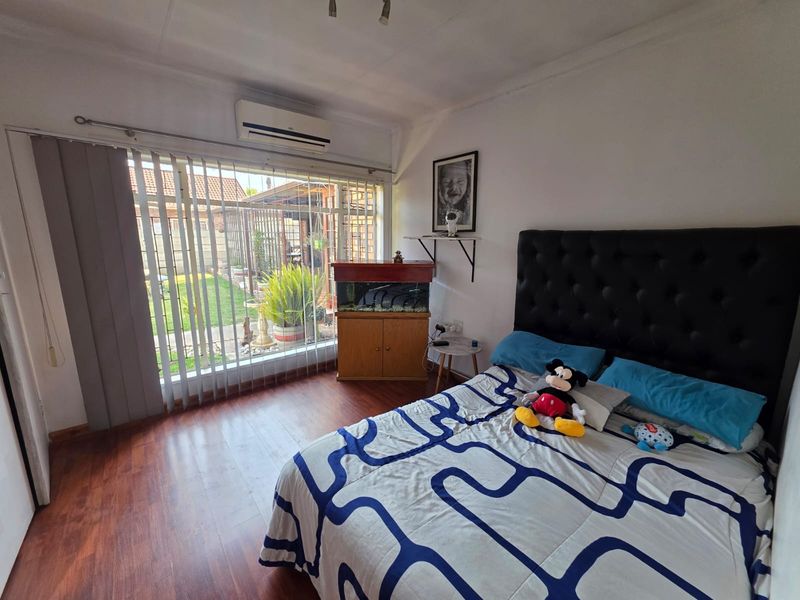 A bedroom featuring laminate flooring, a wall-mounted air conditioning unit, and large sliding glass doors providing access to the rear garden.