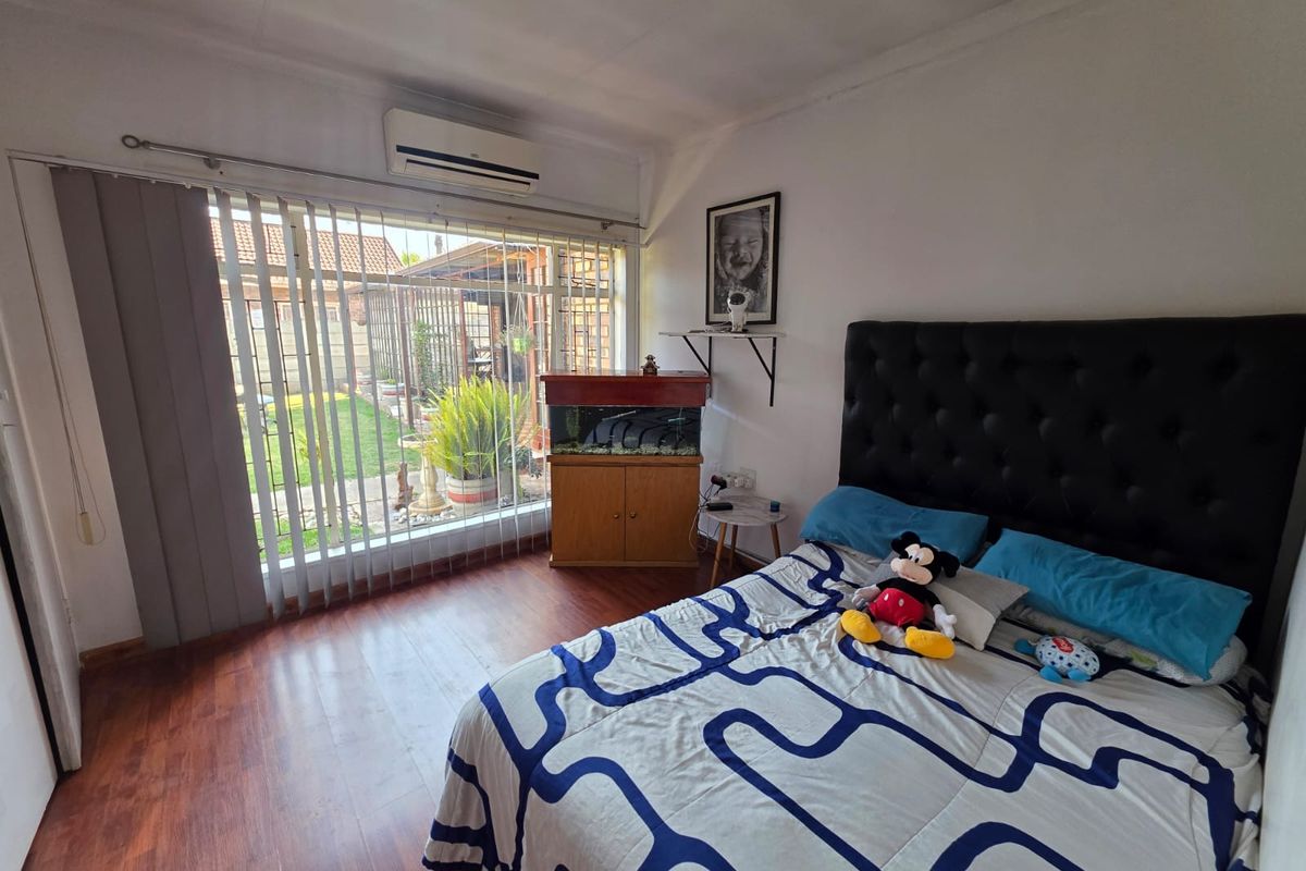A bedroom featuring laminate flooring, a wall-mounted air conditioning unit, and large sliding glass doors providing access to the rear garden.