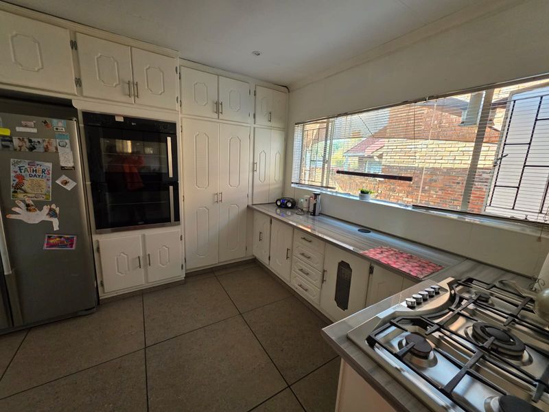 A functional kitchen featuring white built-in cabinetry, a double wall oven, gas hob, and tiled flooring with ample natural light from the large window.