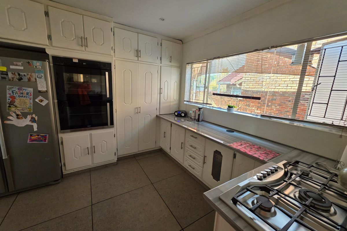 A functional kitchen featuring white built-in cabinetry, a double wall oven, gas hob, and tiled flooring with ample natural light from the large window.