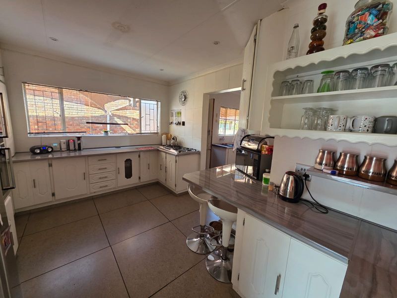 A functional kitchen featuring white cabinetry, laminate countertops, a gas hob, and tiled flooring, with an adjacent scullery area visible.