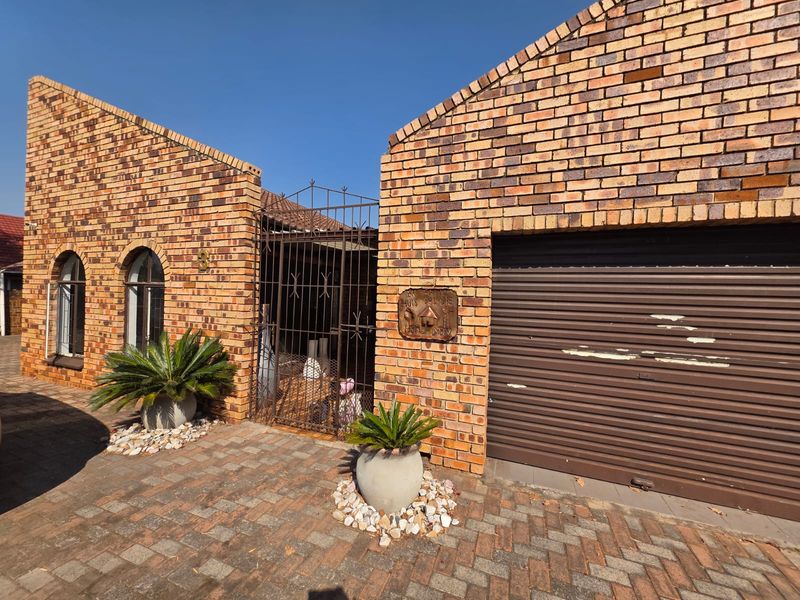 Front elevation of a face brick house featuring a roller garage door, arched windows, and a secure gated entrance with paved driveway.