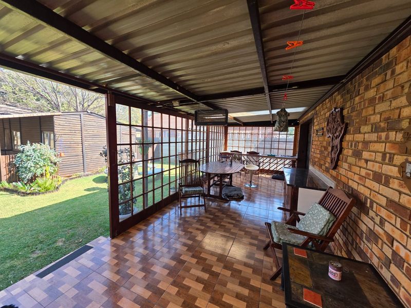 A covered outdoor patio featuring tiled flooring, exposed brick walls, and large glass sliding doors overlooking the garden.