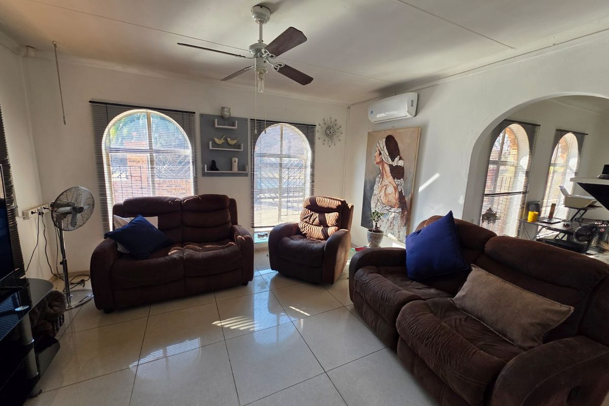 A living room featuring tiled flooring, arched windows, a ceiling fan, and a wall-mounted split-system air conditioner.