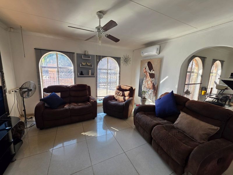 A living room featuring tiled flooring, arched windows, a ceiling fan, and a wall-mounted split-system air conditioner.