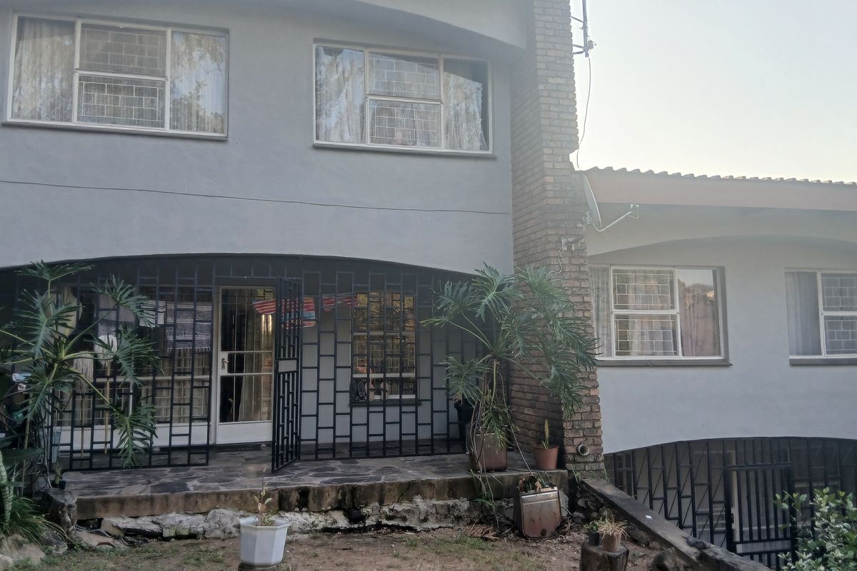 Rear elevation of a multi-level house featuring a stone patio, security gates, and brick chimney detail.