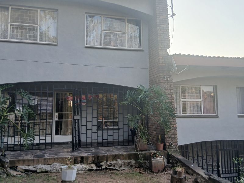 Rear elevation of a multi-level house featuring a stone patio, security gates, and brick chimney detail.