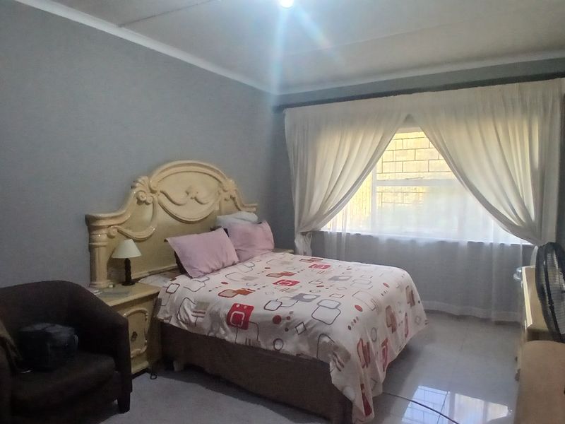 A standard bedroom featuring tiled flooring and large windows with curtain rails, providing a functional living space.