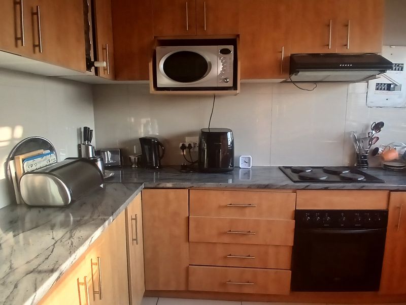 A functional kitchen featuring wood-tone cabinetry, stone-look laminate countertops, built-in oven, electric hob, and an integrated extractor fan with tiled splashback.