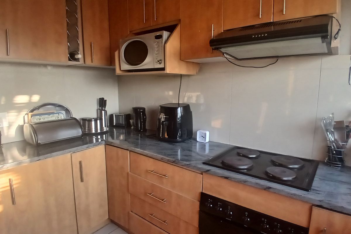 A functional kitchen featuring wood-finish cabinetry, dark laminate countertops, a built-in electric hob, oven, and extractor fan with tiled splashbacks.