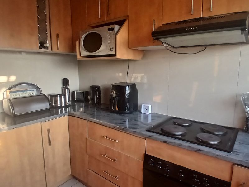A functional kitchen featuring wood-finish cabinetry, dark laminate countertops, a built-in electric hob, oven, and extractor fan with tiled splashbacks.
