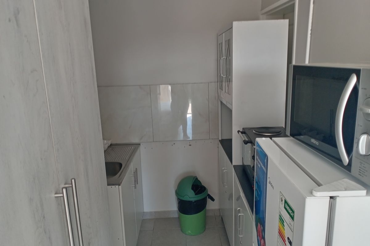 A compact scullery area featuring built-in cabinetry, a stainless steel sink, and tiled splashback, providing functional utility space for the home.